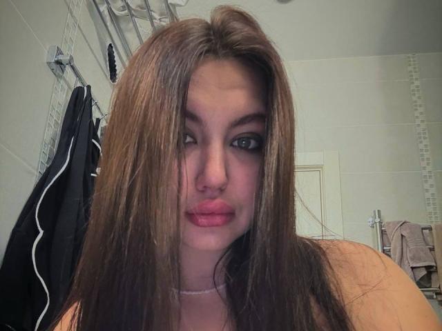 InesGueningsman with wet brown hair, dark eyeliner, and pink lipstick, looking slightly to the side, showing her nose ring and a small, white necklace.
