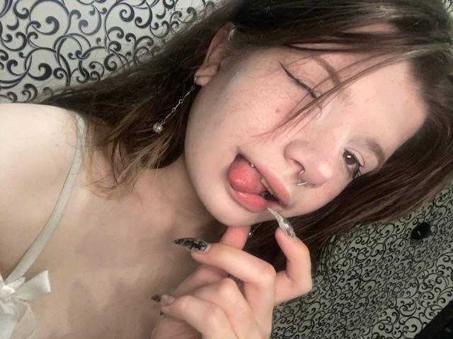 Marla Rotan, met een knipogen, haar tong uit, een neusring en lang bruin haar, houdt een tandenborstel vlakbij haar lippen, en laat haar nagels en sproeten zien. Ze draagt een witte bandeau..