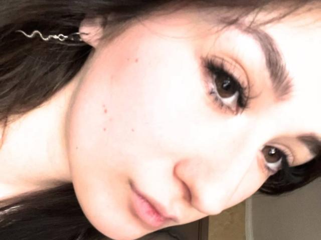 El rostro de Eric Parsygnat, con piel pálida, ojos marrones, pestañas largas y cabello ondulado castaño. Pequeños granitos en la mejilla, una sonrisa sutil y la cabeza ligeramente inclinada..