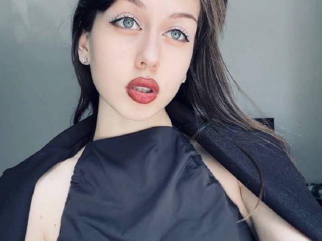 Carrie Sorenson a la peau pâle, les yeux bleus et porte du rouge à lèvres. Elle porte un haut noir sans manches, et ses cheveux bruns foncés sont partiellement visibles..
