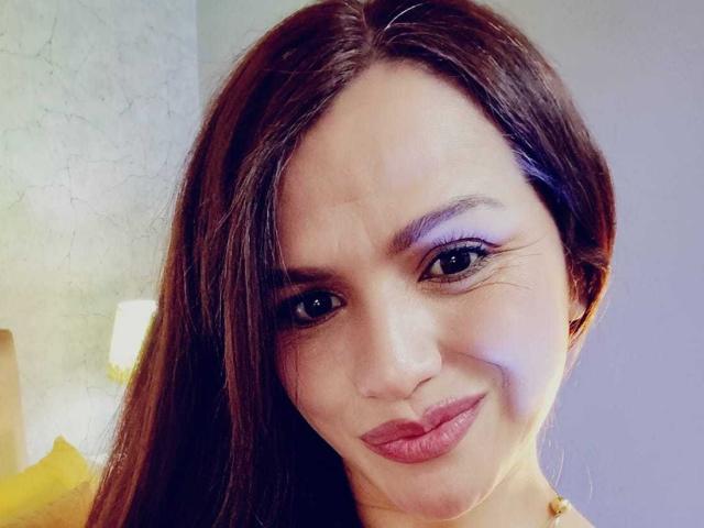 CameronViviane has brown hair, purple eyeshadow, and red lipstick. She's smiling with a slight frown, showing off her pouty ass-kissing lips. Her face is slightly squished.