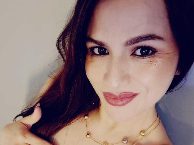 CameronViviane has puffy pink lips, dark brown eyes, and long brown hair, wearing a gold necklace with small beads, smiling at the camera.