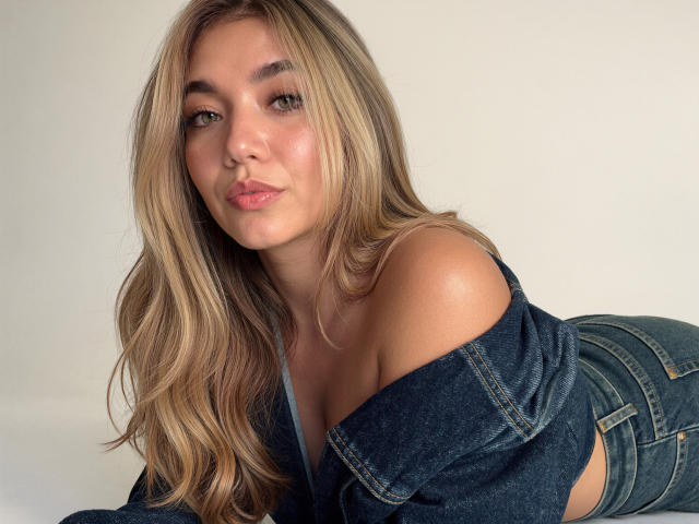 Sofie White, con i capelli biondi, gli occhi verdi e le labbra rosa, sdraiata, indossa una giacca di jeans con una spalla scoperta, mostrando il seno, con dei jeans attillati, e un sorriso appena accennato..