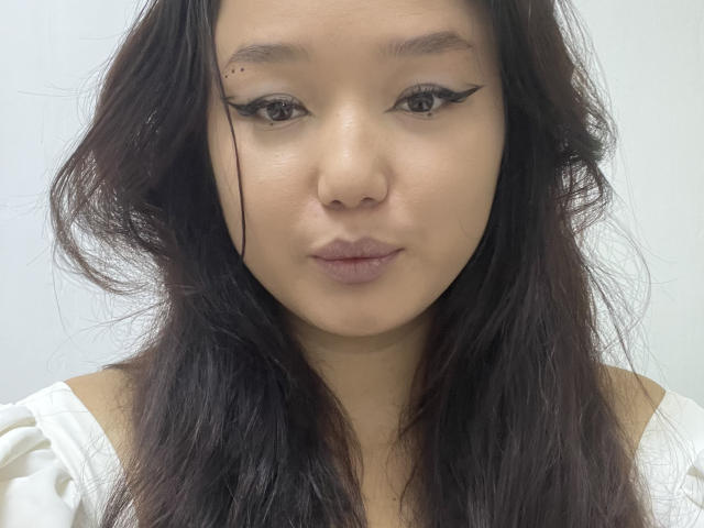 Tayna Harborth a les cheveux noirs et ondulés, une petite tache de beauté au-dessus de son sourcil droit, et elle porte un eye-liner noir en forme d'aile. Elle regarde droit devant elle avec une expression neutre..