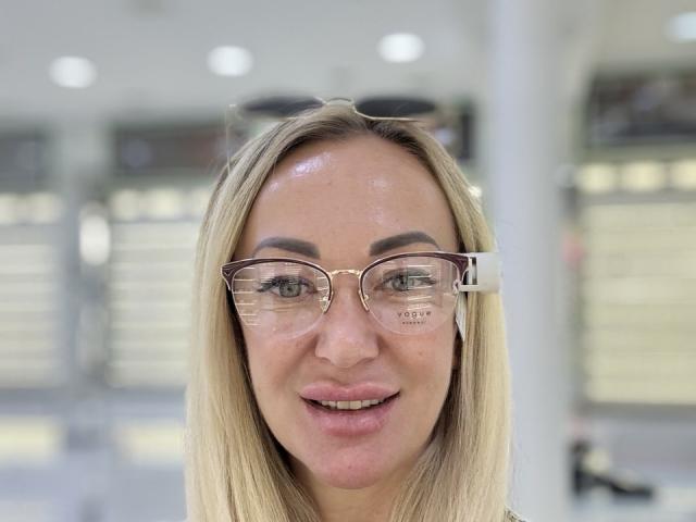 MysteryLaddy has shiny, sweaty skin, wears clear, gold-rimmed glasses, and has blonde hair with a slight side part, smiling with pink lips.