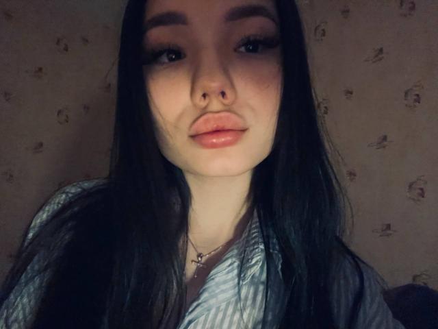 Marge Odum, con i lunghi capelli neri, le labbra piene leggermente aperte e un piccolo piercing al naso, indossa una camicia a righe e ha un viso delicato, leggermente ombreggiato..