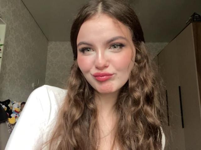 JulienneStradford has wavy brown hair, green eyes, pink lipstick, and a small cut on her right cheek. She's wearing a white top, smiling slightly.