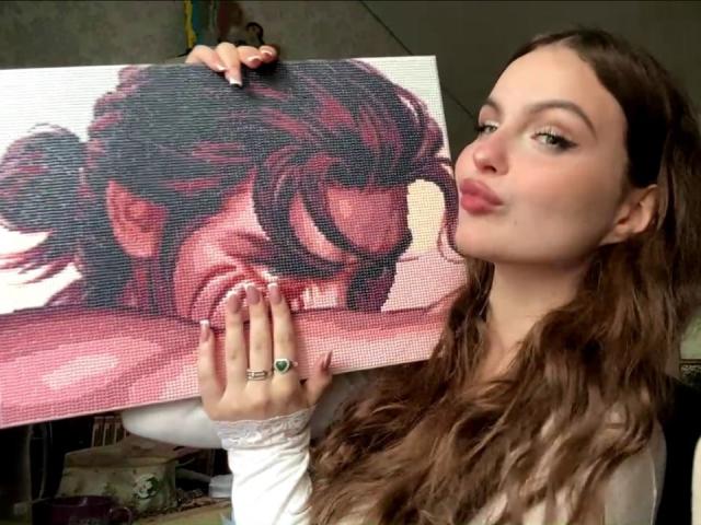 JulienneStradford sosteniendo un retrato de una mujer con cabello rojo oscuro, besándolo, vistiendo una camisa blanca de manga larga, con un anillo en su mano derecha, labios fruncidos..