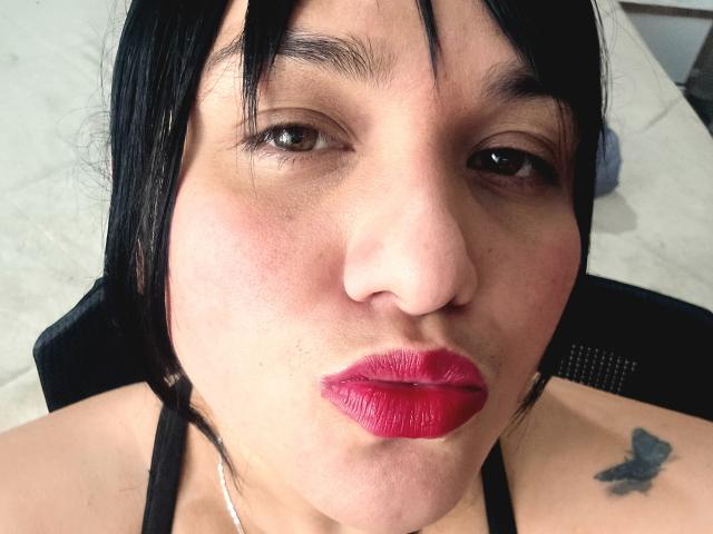 VivianaThompson has puffy red lips, dark straight hair, brown eyes, and a butterfly tattoo on her right shoulder. She's wearing a black halter top.