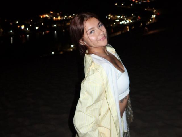 AlessiaFerry with short brown hair, smiling, wearing a white sports bra and yellow jacket, exposing her tits and small tattoo on her side, at night.
