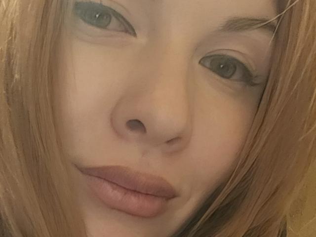 El rostro de KatyBrie, con cabello castaño claro, ojos verdes y labios rosados, ligeramente entreabiertos en una sonrisa relajada y sutil. Su piel es clara y su maquillaje es muy discreto..