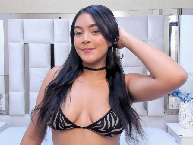 VickyRuiz, com longos cabelos pretos, vestindo um top de biquíni com estampa de zebra, um colar preto e sorrindo, tem a mão no cabelo, mostrando seus seios e seu rosto bonito..