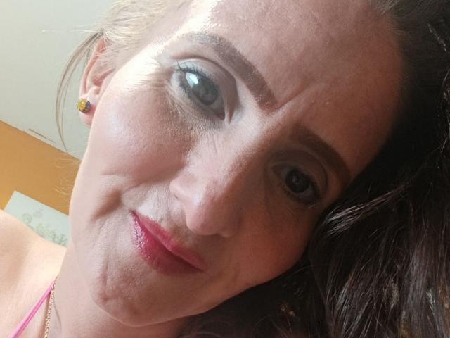 RubiAnderson ha la pelle chiara, i capelli castani ondulati, gli occhi verdi, il rossetto rosa e indossa un top rosa con spalline. Sorride leggermente e indossa una collana d'oro..