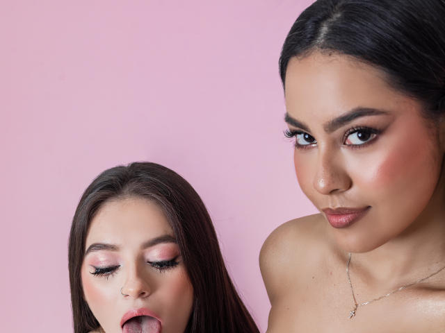 PaolaYKatty, avec des cheveux et du maquillage sombres, la langue tirée, à côté d'une autre PaolaYKatty avec de l'ombre à paupières rose, des cheveux sombres et un sourire discret, toutes les deux topless, sur un fond rose..