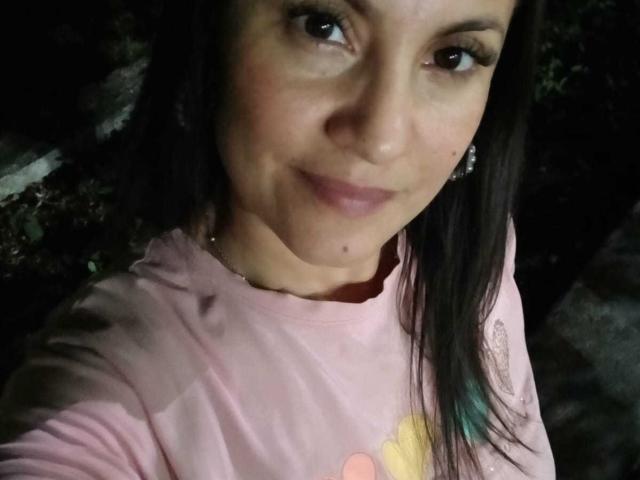 SolaraDubois has dark brown eyes, a small nose, and a slight smile. She's wearing a pink shirt with a yellow design, and has a mole on her chin.