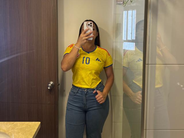 GalaMalkova with medium brown skin, wearing a yellow Brazilian soccer jersey, blue jeans, and a bracelet, taking a mirror selfie, showing her tits and thick ass.