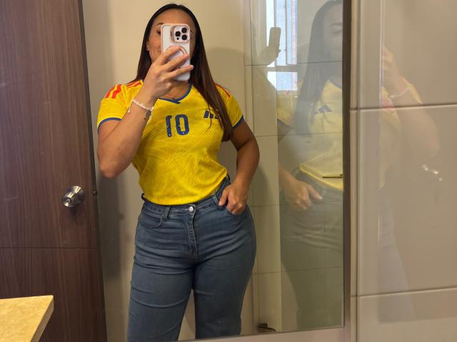 GalaMalkova with long brown hair, yellow football jersey, number 10, blue jeans, holding phone, reflecting in mirror, showing her curvy ass and thick thighs.