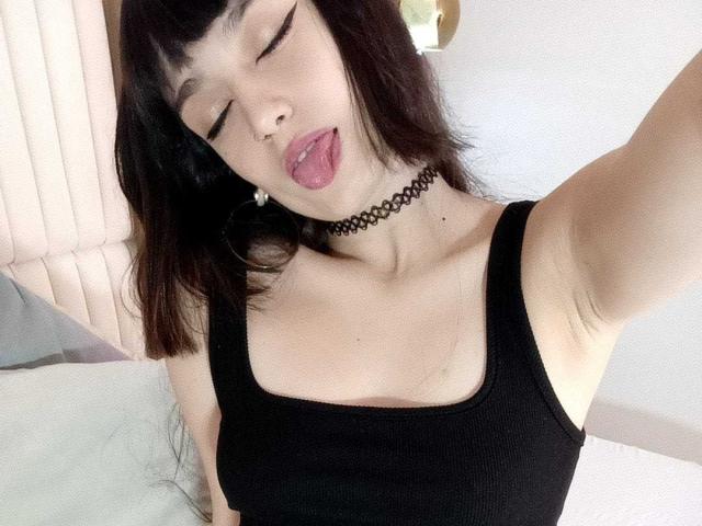 JennInk met een zwarte tanktop, choker, tong uit, ogen gesloten, donkerbruin haar, kleine neusring, bleke huid, zichtbare oksel, zwart haar, kleine borsten, selfie, iets van onderen genomen..