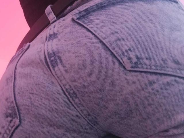 ZarayFeet's Hintern in engen, verwaschenen, blauen Jeans mit sichtbaren Taschen, die Textur und Abnutzung zeigen, unter rosafarbenem Licht..