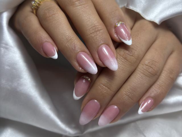Le mani di MiaDuboisX, con unghie curate in stile francese rosa e bianco, un anello d'oro e un piccolo diamante sull'unghia dell'indice, poggiate su seta bianca..