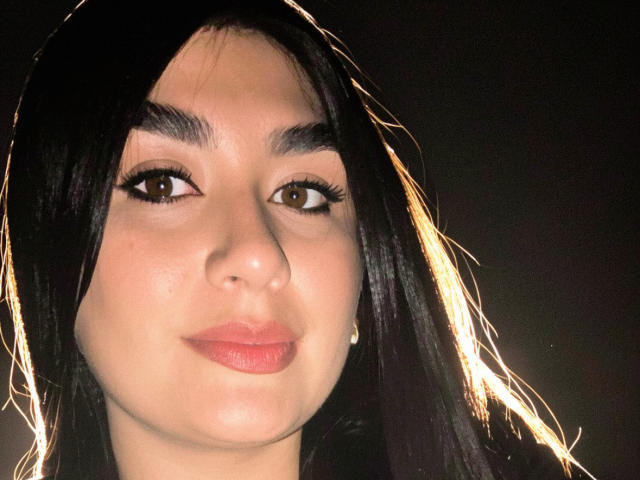 MiaDuboisX ha i capelli neri e lisci, gli occhi marroni e il rossetto rosa. Il suo viso è illuminato lateralmente da una luce calda e brillante. La sua pelle è liscia e chiara..