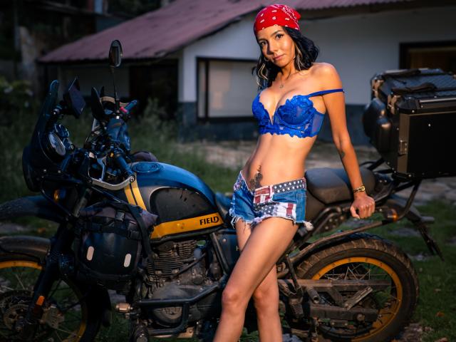 EvelinLuna with blue lace bra, frayed denim shorts, red bandana, and bike, standing next to a black Yamaha motorcycle, showing her tits and a small tattoo on her belly.