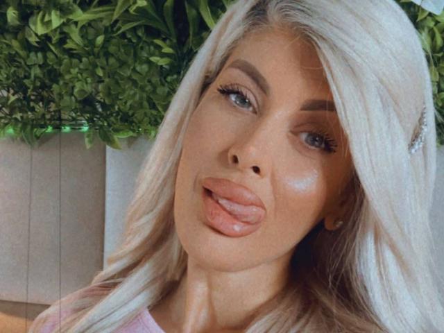 SalmaRoze has long, platinum blonde hair, full pouty lips, and is sticking her tongue out. She's looking at the camera with blue eyes and a slight smile.