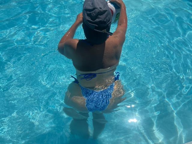 NaomyHott69 ist wieder im Pool, sie trägt einen blauen Bikini-Unterteil und eine schwarze Kappe, mit feuchter, brauner Haut und Wasserwellen um ihrem Hintern und oberen Rücken..