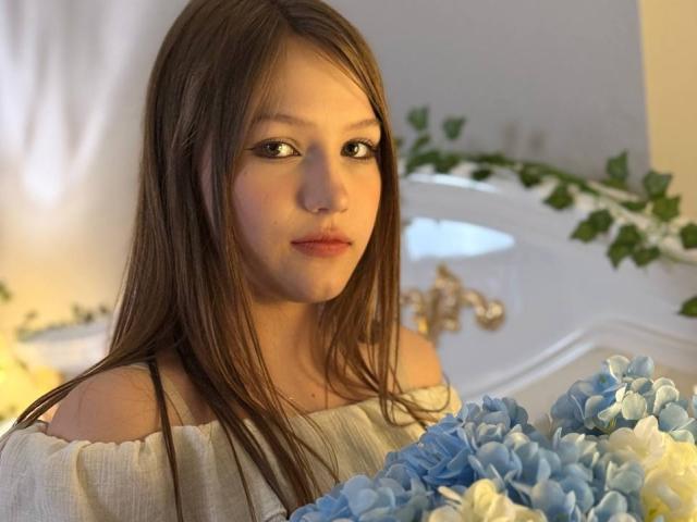 Bubochka with long brown hair, off-shoulder white top, holding blue and white hydrangeas, looking slightly to the side, soft light, gentle expression.