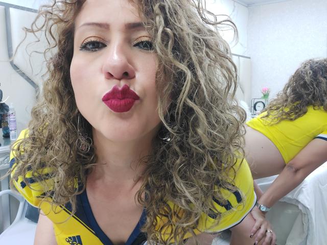 AlexaFireHot with curly blonde hair, red lipstick, and yellow jersey, pouting her lips, wearing a yellow jersey, showing her back and yellow jersey-ass in a mirror.