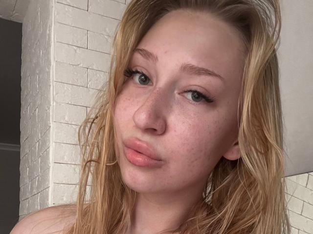 Joette Shigeta heeft blond haar, lichte sproeten en roze lippen. Ze kijkt iets opzij met haar blauwe ogen en lange wimpers. Haar neus is klein en ze draagt geen bovenkleding..