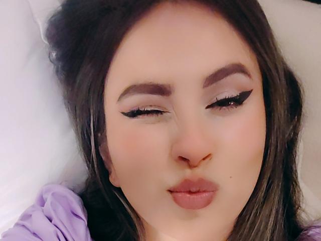 AmiiRosse has pouty lips, half-closed eyelids with sharp black eyeliner, and long brown hair, looking slightly to the side with a soft, pale complexion.