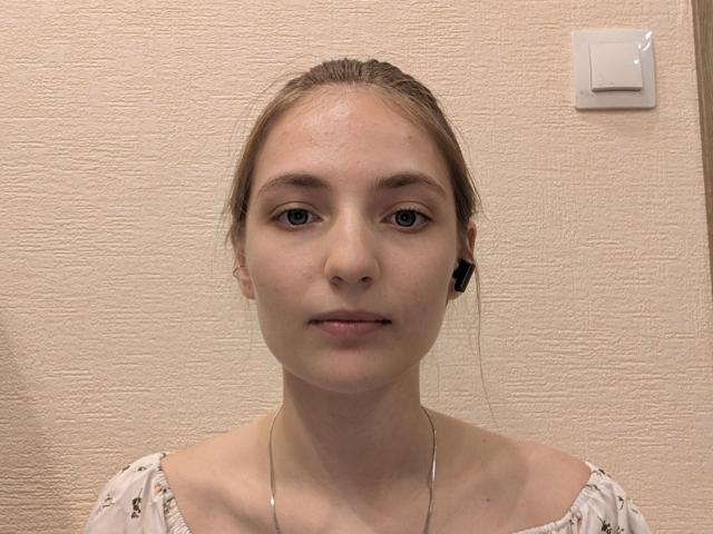 LorindaFinan with fair skin, blue eyes, and light brown hair in a ponytail, wearing a white top with a subtle pattern, has small tits and a silver necklace.