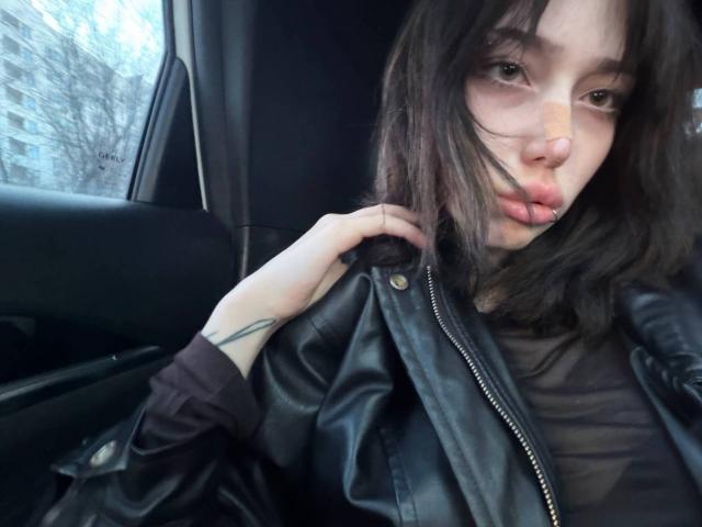 LanHislop, con capelli castano scuro, labbra carnose e un piercing al naso, indossa una giacca di pelle nera, tenendola con una mano tatuata, all'interno di un'auto. Il seno è parzialmente visibile sotto la giacca..