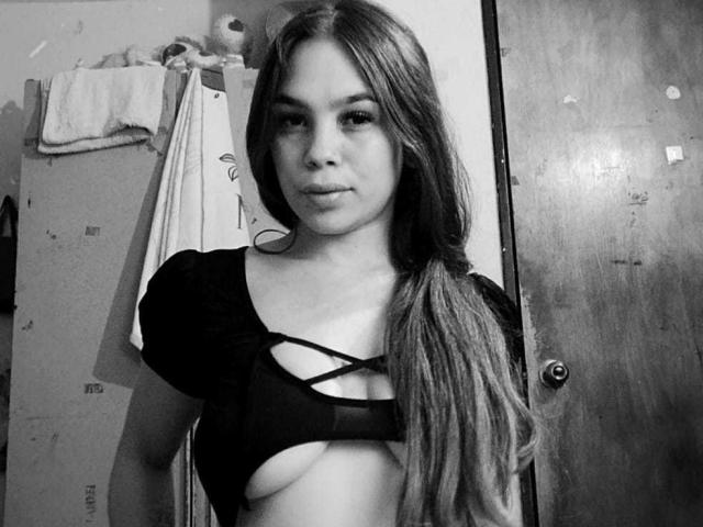 Black-and-white selfie of CloeSantos with long hair, pouty lips, and a revealing top showing her tits through a criss-cross design. She's standing in front of a wooden door.