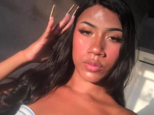 BabeSoffia, con la pelle luminosa, i capelli scuri e ondulati e le unghie lunghe, fa la smorfia con le labbra rosa leggermente dischiuse, illuminata dal sole e sudata. Le sue sopracciglia sono folte e sta tenendo i capelli..
