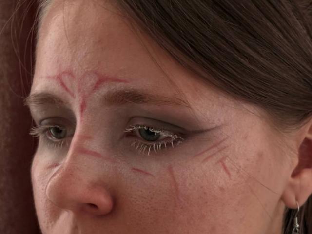 Il viso di Johnetta Urtiaga presenta dei graffi rossi sulla fronte, sulle sopracciglia e sulla guancia, ha gli occhi verdi, i capelli castani e un leggero cipiglio. Il suo trucco include un eyeliner ad ali di gabbiano..