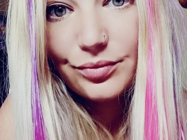 AlmaDeAngel69 ha i capelli biondi con riflessi rosa e viola, un anello al naso e gli occhi azzurri. Le sue labbra rosa sono leggermente dischiuse in un sorriso appena accennato..