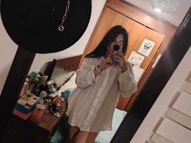 ZoeyGrey takes a mirror selfie in a bedroom, wearing an oversized white shirt, showing her bare thighs, with her phone covering her face and long black hair.