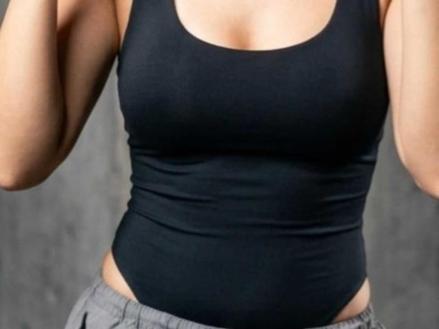 Le débardeur noir de SharonBellarie épouse ses seins, dévoilant une poitrine généreuse, tandis que son pantalon gris est juste au-dessus de ses fesses. Ses bras sont levés, coupant à hauteur des épaules..