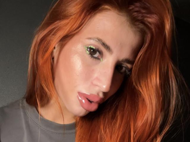 RosioRaschko heeft glanzend, nat uitziend rood-oranje haar, groene oogschaduw en glanzende roze lippen, met een subtiele, sexy, verleidelijke uitdrukking. Haar gezicht is licht naar links gekanteld..