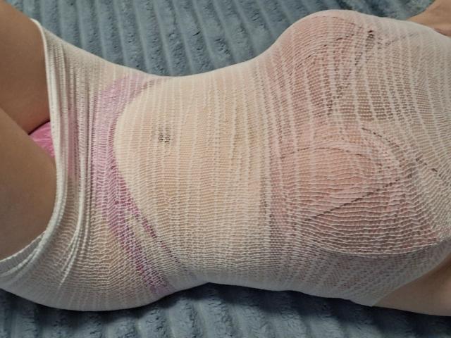 La maglia bianca in rete di Marriam, aderente sul seno e sui glutei, leggermente trasparente, rivela un reggiseno rosa sottostante, adagiata su una superficie blu con texture..