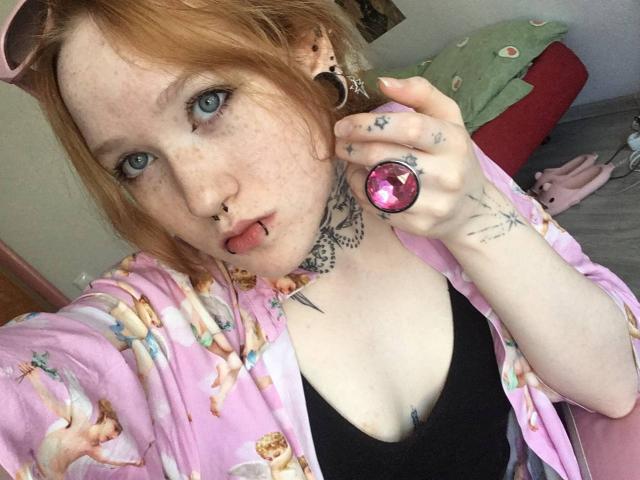 Machelle Trebesch heeft rood haar, sproeten en blauwe ogen. Ze steekt haar tong uit, draagt een roze bloemenbadjas, een zwart tanktopje en een roze ring, en heeft tatoeages..
