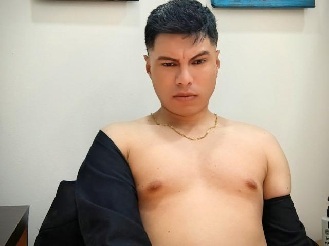 AquilesTaylor is a shirtless Asian man with short black hair, a gold chain, and a serious expression. He has small nipples and a black jacket off his shoulders.
