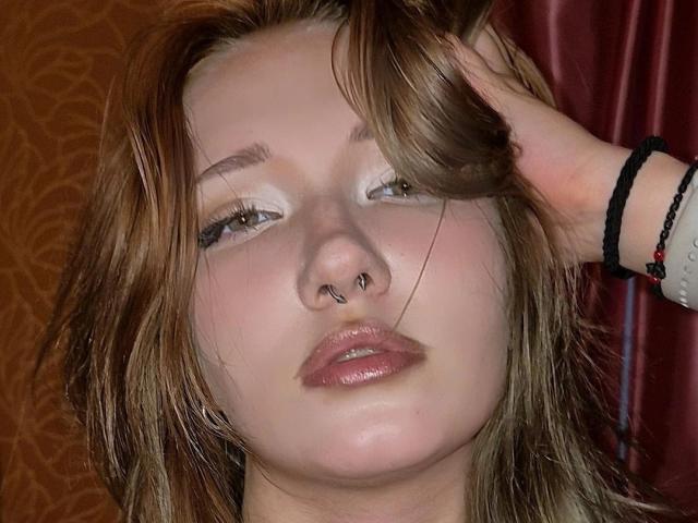 PalmiraEsquinaldo tem cabelos castanhos desalinhados, um piercing no nariz e lábios rosados brilhantes, com uma mão no cabelo e uma pulseira preta no pulso..