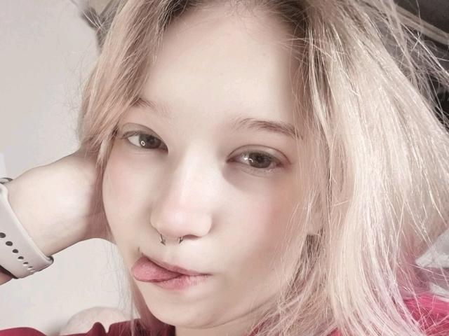 PalmiraEsquinaldo tem pele clara, cabelo loiro e um piercing no nariz. Ela está de língua para fora, usando um smartwatch branco e tem uma aparência um pouco desarrumada..