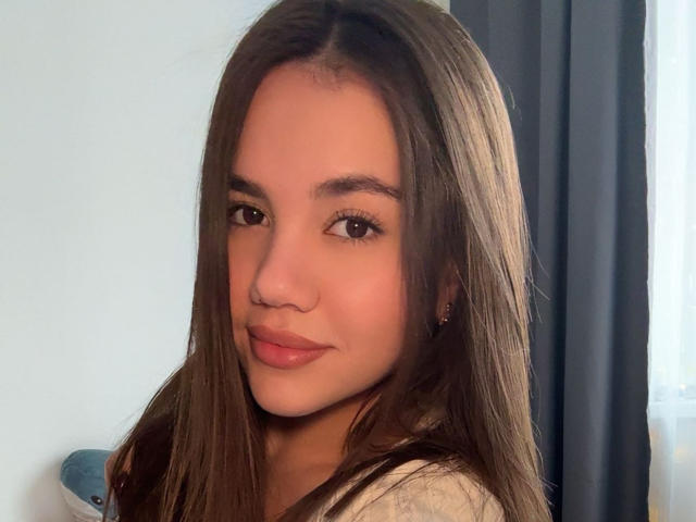 Santina Schaumberg tiene el pelo largo y castaño, un aro nasal bonito, y está sonriendo con labios rosados y brillantes. Está mirando a la cámara con ojos marrones. Sus senos no son visibles..