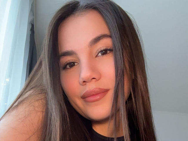 El rostro de Santina Schaumberg, con cabello largo y castaño, ojos marrones, labios carnosos y una ligera sonrisa. Tiene una nariz linda y lleva puesto un top negro..