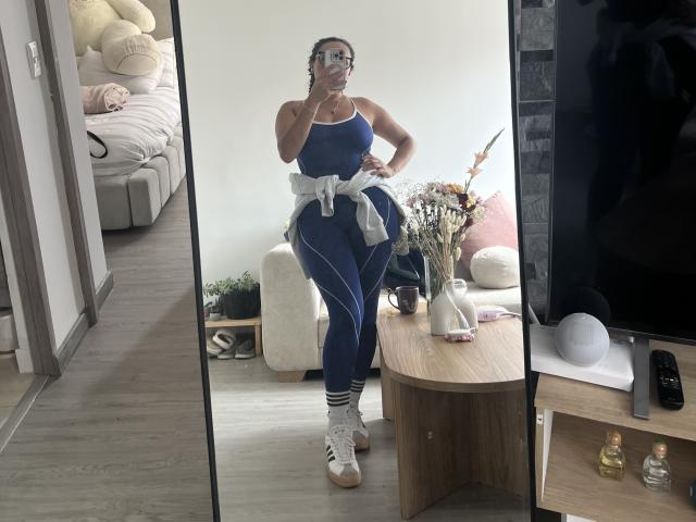 GalaMalkova, wearing a blue sports bra and matching leggings, white sneakers, and a gray tied top, standing in front of a mirror, showing off her toned ass.