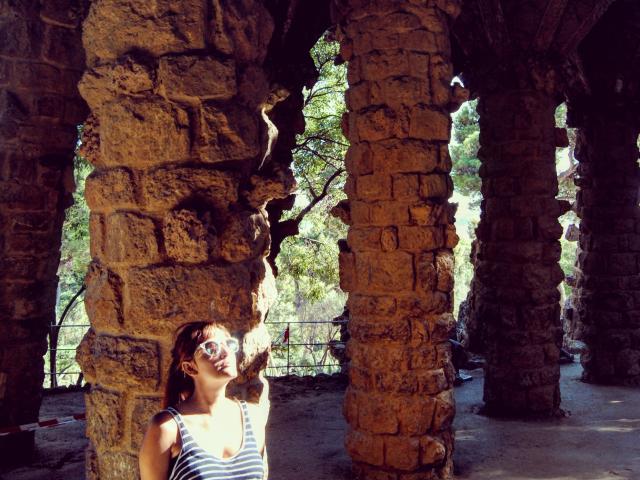 JaneRoa, com seios pequenos, vestindo uma regata listrada, apoiada em um pilar de pedra, usando óculos de sol, com a luz do sol filtrando, arco de pedra, textura de rocha, luz da floresta, pose relaxada..
